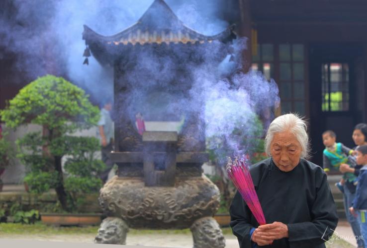 一位头发雪白凌乱的老婆婆虔诚地焚香祷告,祈求菩萨保佑.